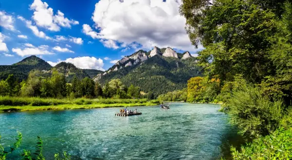 Flöße auf einem türkisfarbenen Fluss vor bewaldeten Bergen. Ein idyllisches Bild für Ausflugsziele Polen.