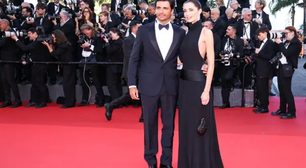 A couple in formal wear on a red carpet, surrounded by photographers.