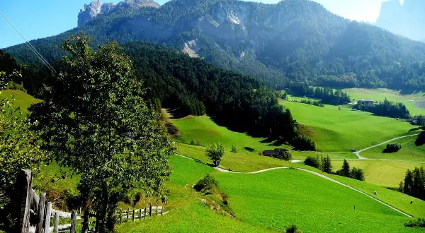 Verdi colline e montagne maestose incorniciano i pittoreschi paesi del Val di Funes, con un sentiero che serpeggia tra prati lussureggianti.