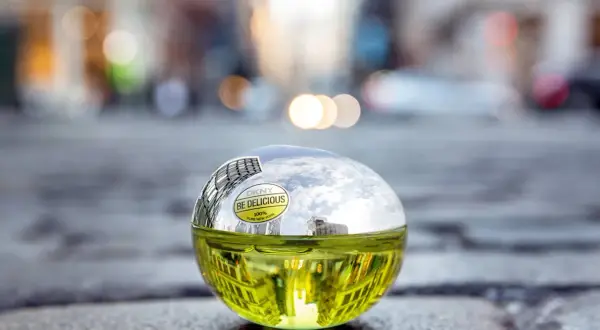 DKNY Be Delicious 100 ml, zielony flakon perfum w kształcie jabłka, odbijający miejski krajobraz.