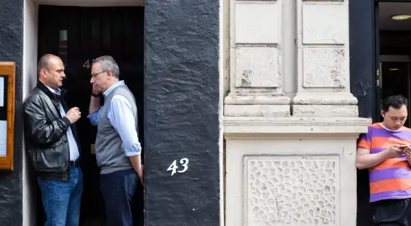 50mm street photography captures two men in conversation by a doorway numbered 43, while another man looks at his phone.