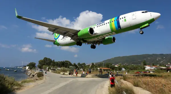 Ett flygplan landar lågt över vägen vid Skiathos flygplats. Människor står längs vägen och tittar upp.