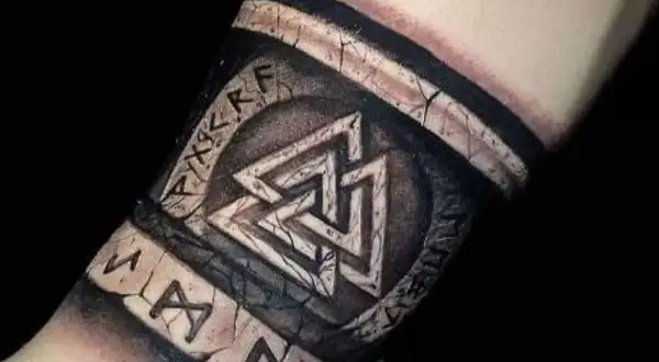 Tatuaże wikingów na przedramieniu: symbol Walhalla i runy, wyglądające jak wyryte na kamieniu.