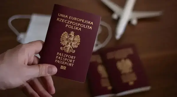 Dłoń trzyma polski paszport. Obok leżą kolejne dokumenty, maseczka i samolot. Zastanawiasz się, ile się czeka na paszport?
