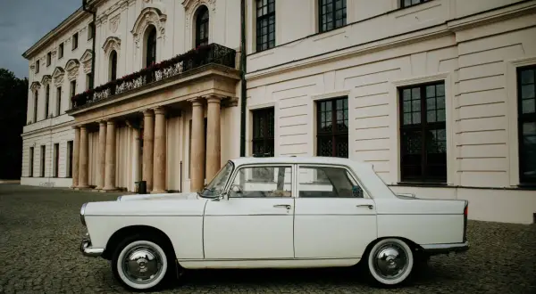 Biały Peugeot 404 na brukowanym dziedzińcu przed pałacem.