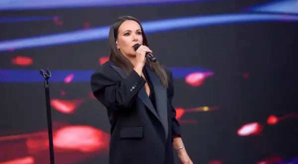 Kasia Kowalska w czarnej marynarce śpiewa na scenie, wykonując swoje utwory.