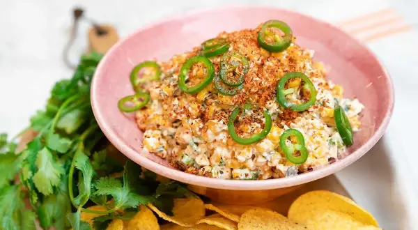 En krämig mexikansk majssallad toppad med jalapeños och serverad med tortillachips och färsk koriander.