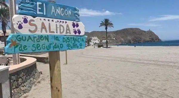 Cartel en la playa El Ancón, Carboneras: "Salida. Guarden la distancia de seguridad". Palmera y mar al fondo.