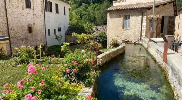 Un ruscello attraversa un borgo umbro, tra case in pietra e rose rosa. Un angolo incantevole tra i borghi più belli dell'Umbria.