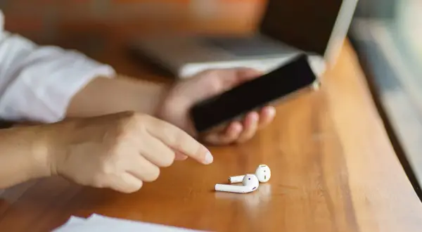 Osoba trzyma telefon, obok leżą białe słuchawki. Może to być powód, dla którego dźwięk przez Bluetooth przerywa na Androidzie.