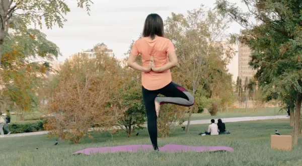 Mujer en postura de árbol, practicando yoga al aire libre en un parque.