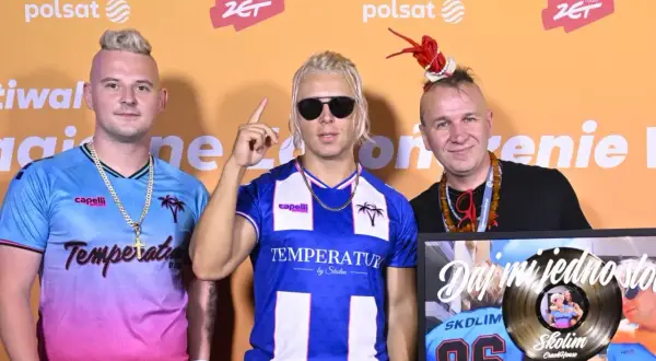 Trzech mężczyzn pozuje do zdjęcia. Jeden z nich trzyma złotą płytę.