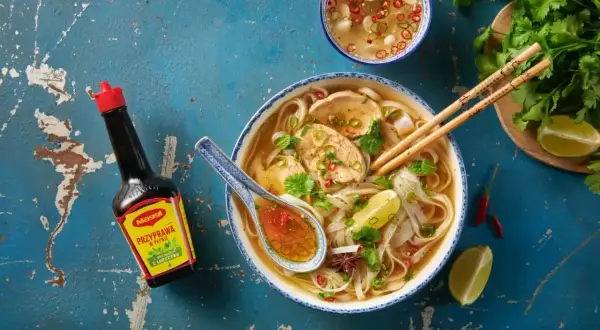 Aksamitny makaron pho z kurczakiem, świeżą kolendrą i limonką. Obok sos Maggi i miseczka z dodatkami.