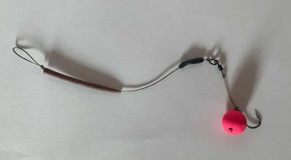 Ein **hinged stiff rig** mit einem pinken Pop-up Boilie und einem Haken.
