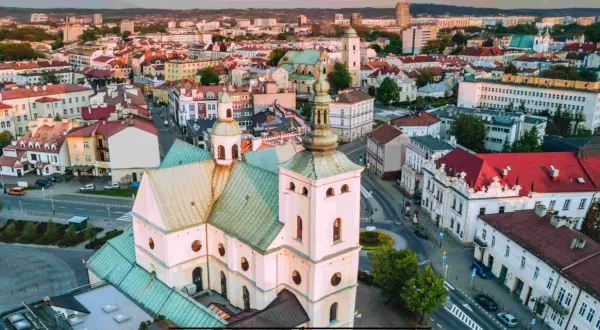 Widok z lotu ptaka na rzeszów rynek z dominującą białą bazyliką i zielonymi dachami. W tle zabudowa miejska.