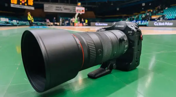 Profesjonalny obiektyw Canon EOS R1 z teleobiektywem 70-200mm na zielonej podłodze hali sportowej.