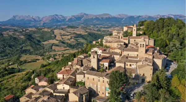 Borgo medievale di Penna San Giovanni, con le sue case in pietra e i tetti in cotto, incastonato tra dolci colline e montagne maestose.