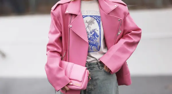 Giacca rosa in ecopelle, che dimostra il suo significato di alternativa sostenibile alla pelle animale. Borsa coordinata e jeans.
