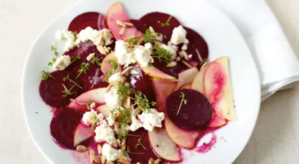 Ein köstlicher rote beete salat mit Apfelscheiben, zerbröckeltem Käse, Sonnenblumenkernen und Kresse garniert.