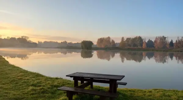 Poranek nad jeziorem, idealne miejsce na dzikie łowiska mazowieckie. Drewniana ławka i stół czekają na wędkarzy.