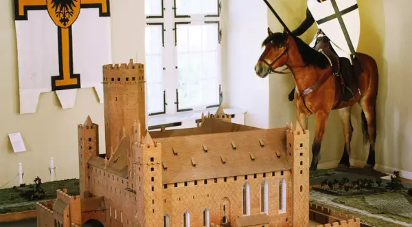 Ein deutscher Orden Ritter auf einem Pferd, mit Lanze und Schild, steht vor einem Modell einer mittelalterlichen Burg.