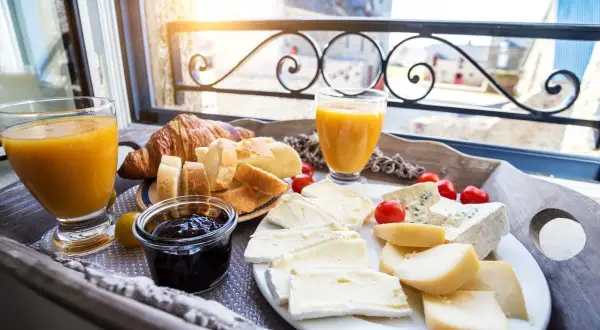 Idealne francuskie śniadanie: świeży rogalik, pieczywo, sery, dżem i sok pomarańczowy na tacy przy oknie.