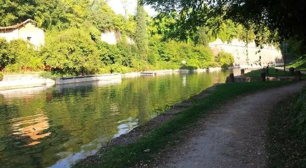 Sentiero lungo il canale, ideale per la ciclabile Peschiera Mantova. Vegetazione lussureggiante e riflessi sull'acqua.