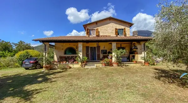 Una casa di campagna con un'auto parcheggiata, piante in vaso e un prato verde. Il momento perfetto quando comprare casa.