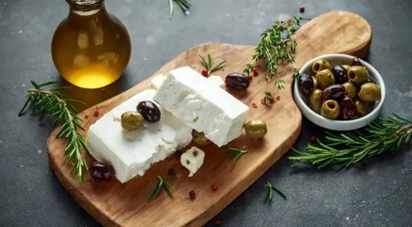 Kostki sera feta, oliwki, rozmaryn i oliwa z oliwek na desce. Idealne do sałatki, a feta kcal nie są tak wysokie.