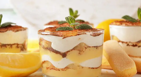 Délicieux tiramisu citron, superposé dans des verres avec des biscuits à la cuillère et des citrons frais.