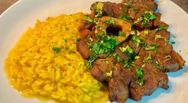 Ossobuco alla milanese succulento su un letto di risotto giallo brillante, guarnito con prezzemolo fresco.