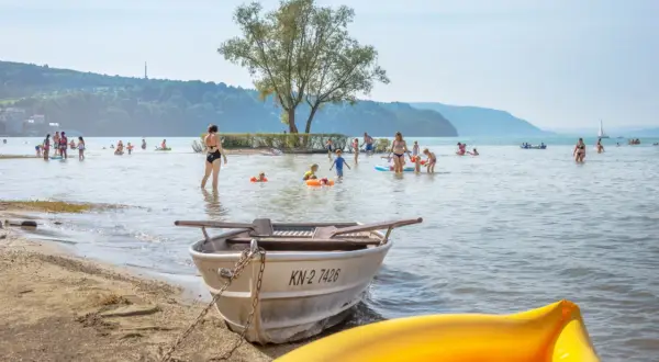 Sommerlicher Trubel am **Konstanz Bodensee Strand**: Familien planschen, Kinder spielen im Wasser, Boote liegen am Ufer.