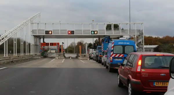 Voiture rouge et camions bleus dans une file d'attente au péage flux libre A13. Lumières rouges et vertes sur les panneaux.