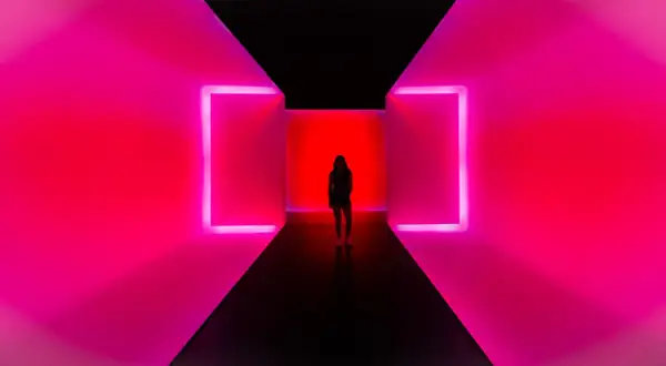 Kobieta stoi w korytarzu z neonowym oświetleniem. To nowoczesne instalacje artystyczne, które tworzą hipnotyzującą grę światła i koloru.