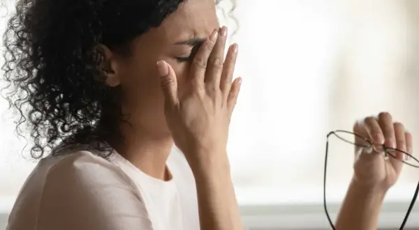 Frau reibt sich die Augen, hält Brille in der Hand. Sie fühlt sich erschöpft, vielleicht wegen **Schwindel durch Stress**.