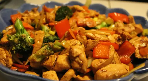En blå skål fylld med wokad kyckling, broccoli, paprika och morötter. En läcker och färgstark måltid.