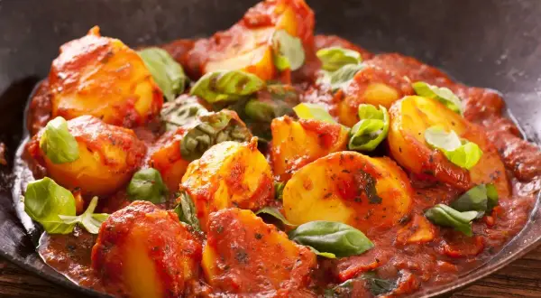 Patate al sugo, un delizioso contorno per carne alla pizzaiola, guarnite con basilico fresco.