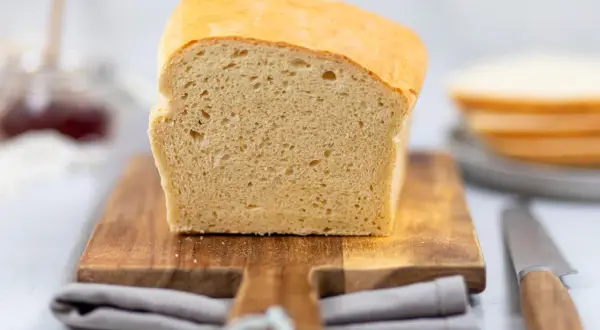 Frisch gebackenes Toastbrot, perfekt für Ihr nächstes Toastbrot Rezept. Auf einem Holzbrett mit Messer und Marmelade im Hintergrund.