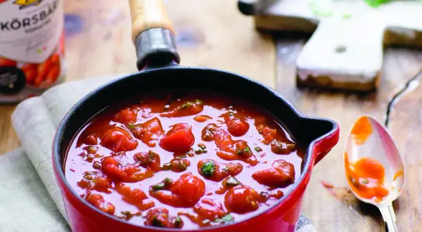 En röd gryta fylld med en hemlagad tomatsås, perfekt för ditt nästa tomatsås recept. En sked med sås ligger bredvid.
