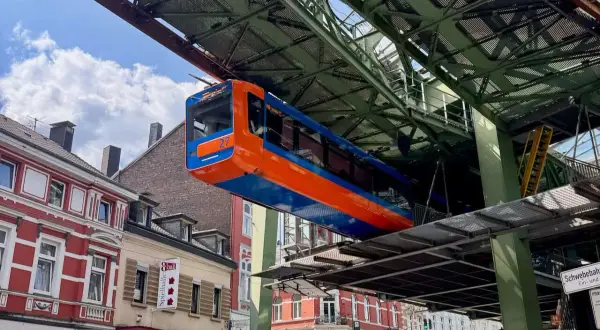 Die orange-blaue Schwebebahn fährt über den Dächern von Wuppertal.
