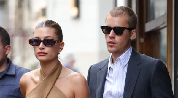 Hailey Bieber und Justin Bieber, beide mit Sonnenbrillen, wirken semi-formal. Sie spazieren durch die Stadt, sie in einem braunen Top, er im Anzug.