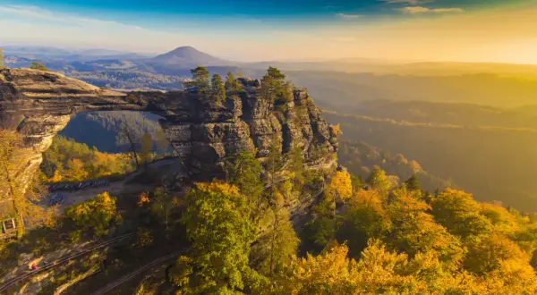 Skalny most Pravčická brána w Czechach, idealne miejsce na weekendowy wypad. Jesienne kolory lasów i zachodzące słońce tworzą magiczny widok.