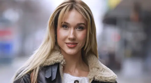 Uśmiechnięta blondynka w brązowej kurtce ze sztucznym futrem, przypominającej strój diablicy, pozuje do zdjęcia.