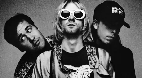 Drei Mitglieder von Grunge-Bands posieren für ein Schwarz-Weiß-Foto. Der Frontmann trägt auffällige weiße Sonnenbrillen.