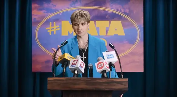 Mata w niebieskiej marynarce przemawia za mównicą z mikrofonami, na tle napisu "#MATA".