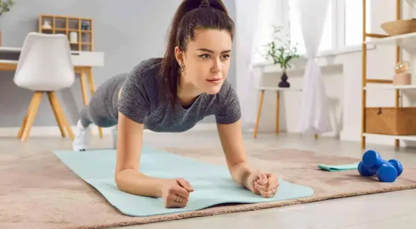 Donna in posizione di plank, parte di un allenamento metabolico casalingo. Sul tappetino, manubri blu.