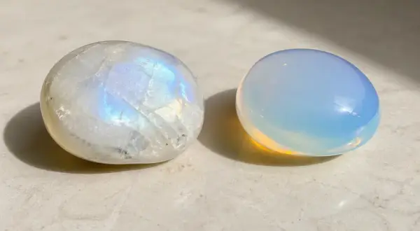 Dos piedras pulidas, una piedra luna iridiscente y otra de un azul lechoso, descansan sobre una superficie clara.