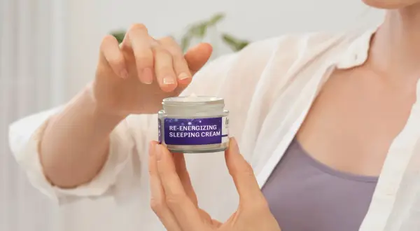 Hände halten ein Glas "RE-ENERGIZING SLEEPING CREAM". Für jugendliche Haut braucht man eine Nachtcreme.
