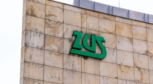 Zielone logo ZUS na beżowej, kamiennej elewacji budynku.