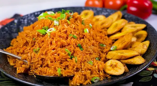 En stor portion jollof rice med stekt plantain, garnerad med salladslök. En härlig måltid!